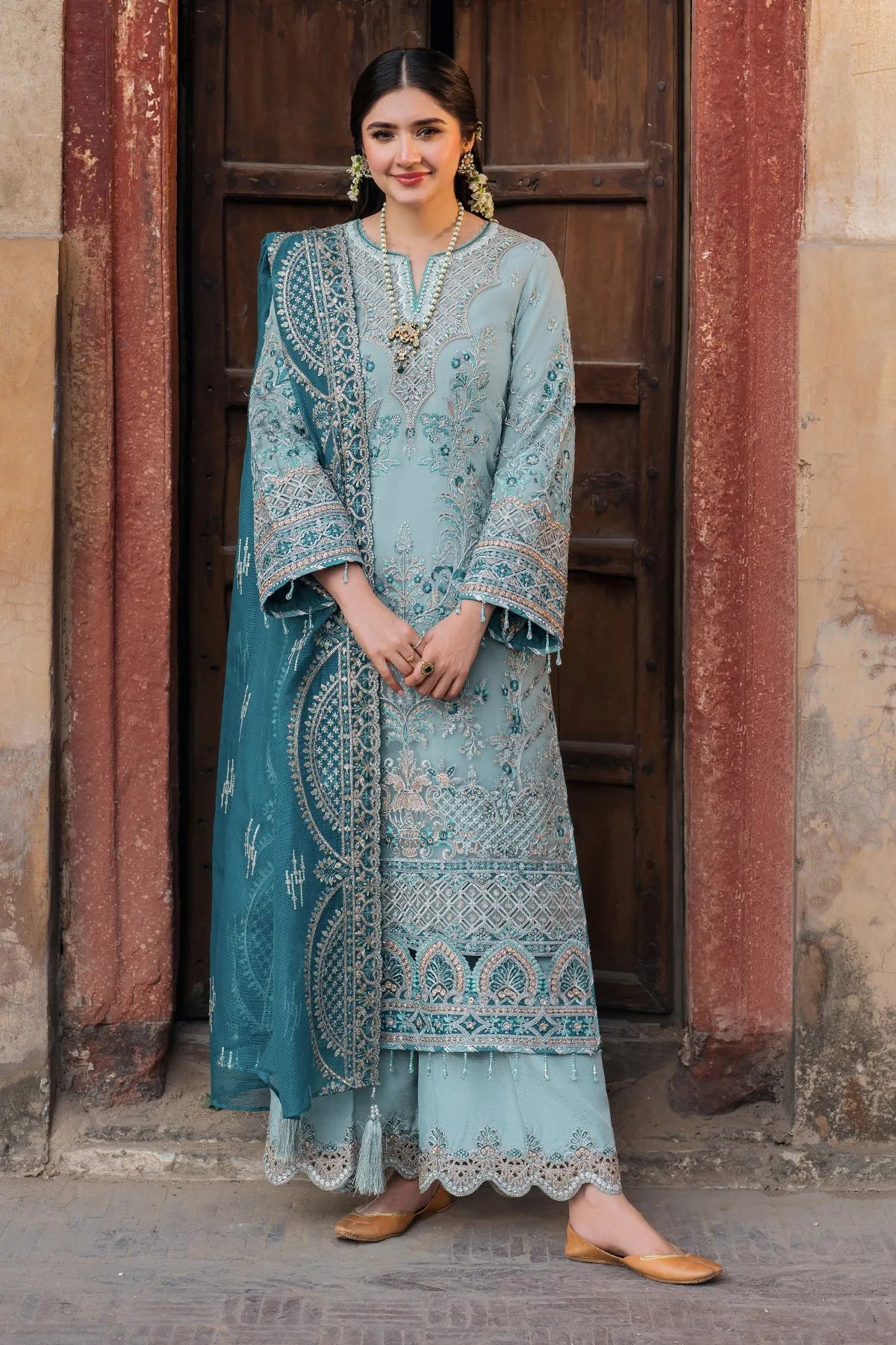 A woman wearing a blue and white embroidered organza three-piece ensemble with a dupatta and trousers.