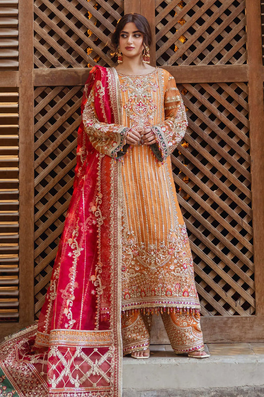 A woman wearing a traditional, embroidered red and orange outfit with a dupatta, standing in front of a paisley patterned backdrop.