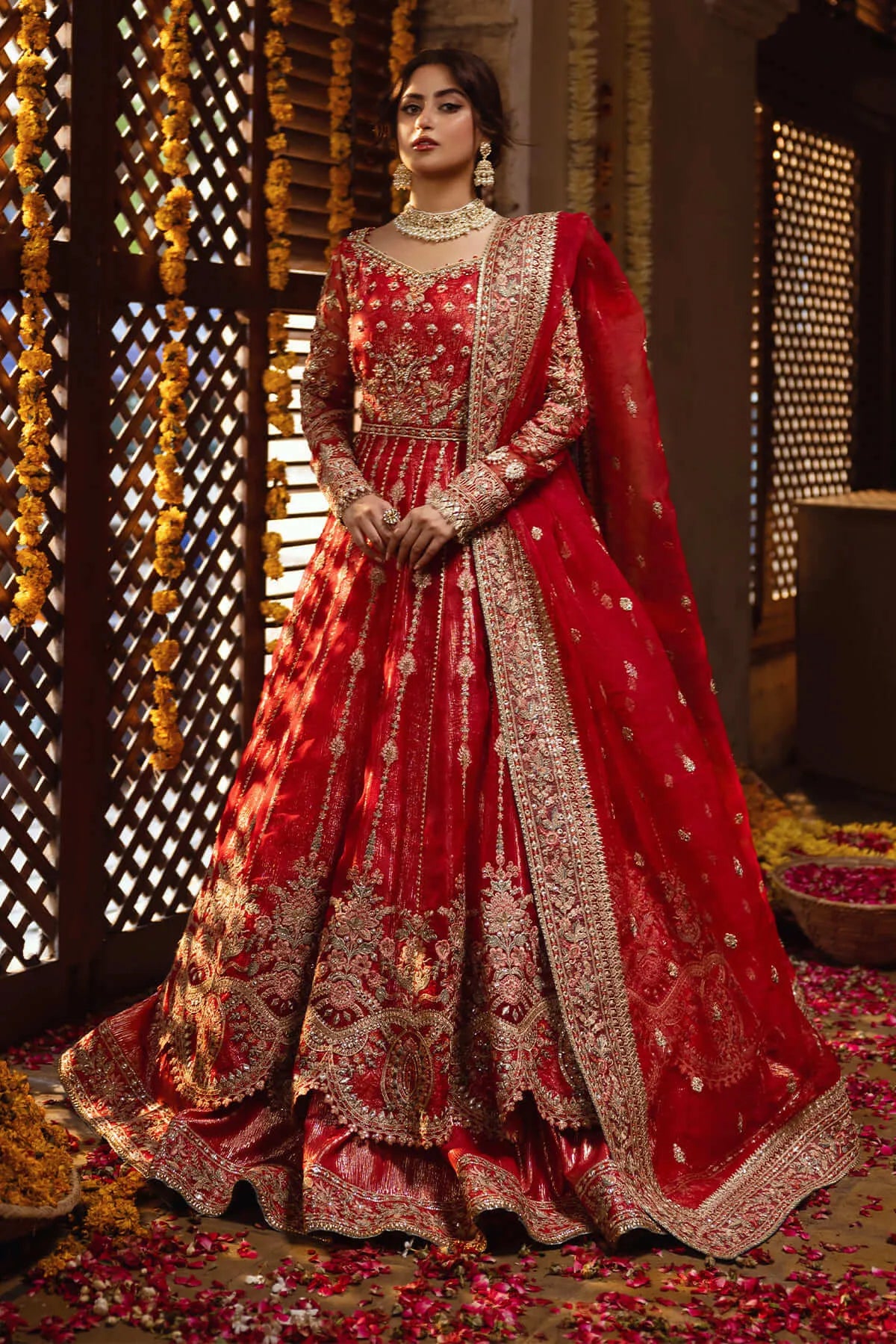 A woman wearing a traditional red and gold bridal lehenga with detailed embroidery and organza borders.