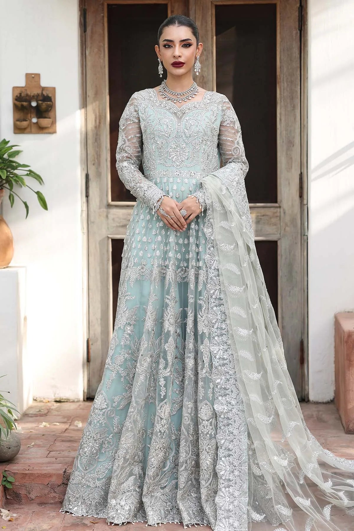 Woman in a light blue embroidered traditional outfit standing outdoors.