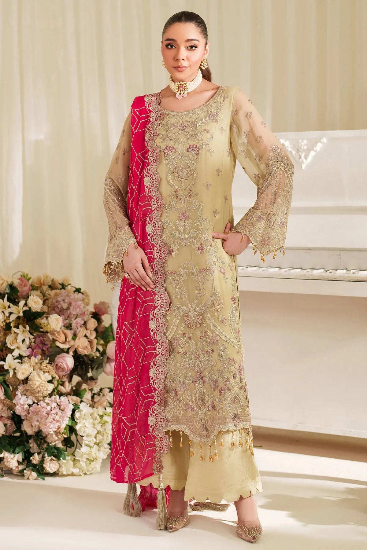 Woman in a traditional outfit with a pink dupatta standing in a decorated room.