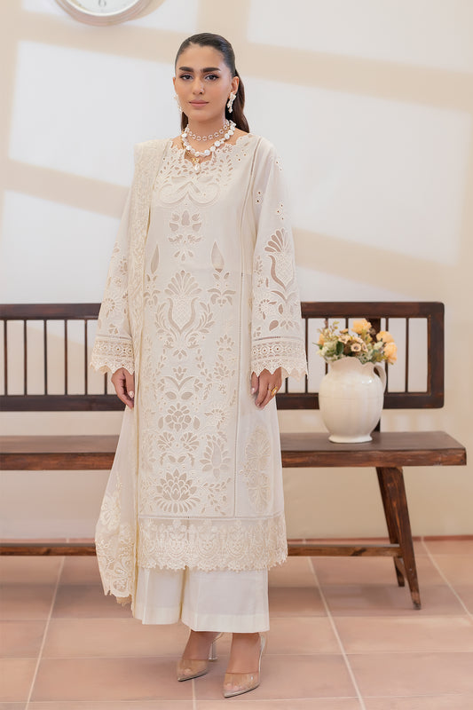 Woman in a white embroidered outfit standing in a room with a wooden bench and vase.
